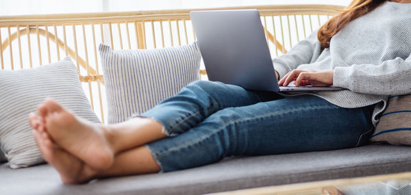 Low section of woman using laptop while sitting on bed at home