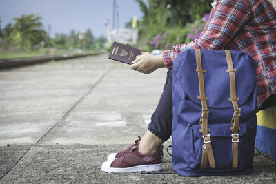 Low section of man with passport sitting on footpath