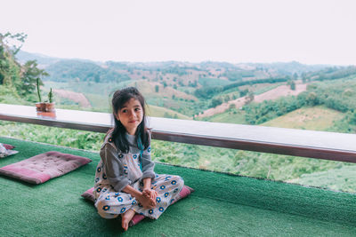 A beautiful asian girl sitting on balcony and looking at mountains and green