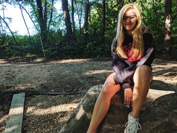 Portrait of smiling young woman sitting on rock in forest