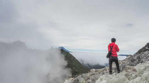 Rear view of man standing on rock against sky