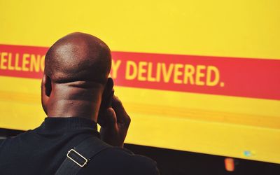 Rear view of man with shaved head standing against yellow wall