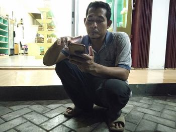 Young man using mobile phone while sitting on floor