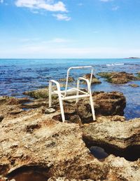 Deck chairs on rocks by sea against sky