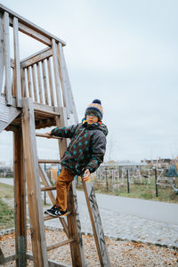 Portrait of boy standing on ladder against sky in playground