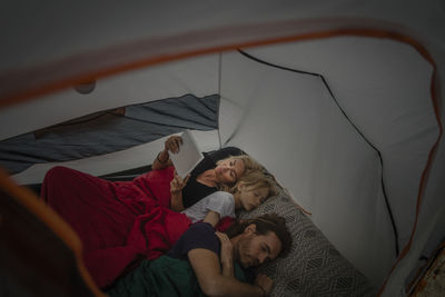 High angle view of mature woman using digital tablet while lying with family in tent