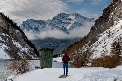 Rear view of man standing at lakeshore during winter