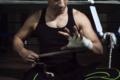 Midsection of athlete wrapping hands with bandage in gym