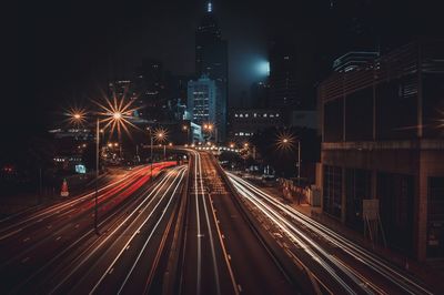 Light trails on road by illuminated buildings at night