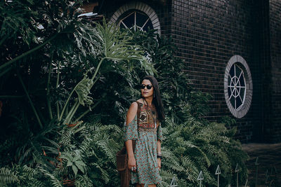 Woman wearing sunglasses while standing by plants