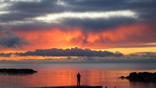 Silhouette person by sea against sky during sunset