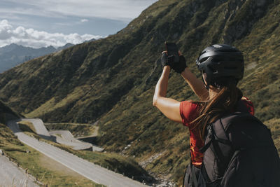 Woman wearing helmet photographing gotthard pass through smart phone on sunny day