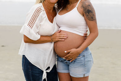 Mom and pregnant daughter embrace, baby belly close up