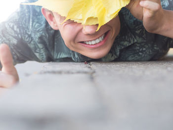 Surface level of happy man face covered with yellow autumn leaves on walkway