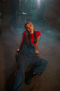 Portrait of beautiful young woman sitting on floor amidst smoke