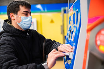 Side view of blind male in medical mask paying for ticket in terminal in metro