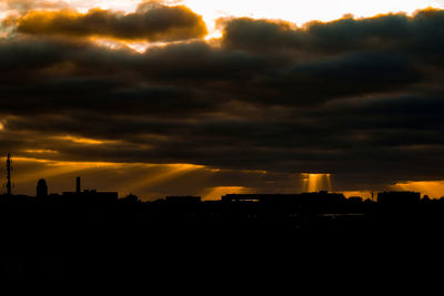 Silhouette buildings against cloudy sky during sunset