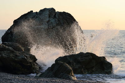 Sea waves splashing on rock against sky