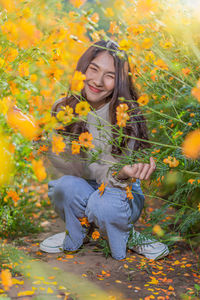 Full length of woman crouching by yellow flowering plants