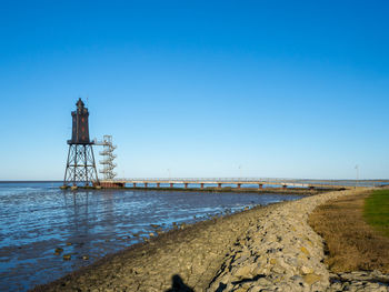 Lighthouse by sea against clear blue sky