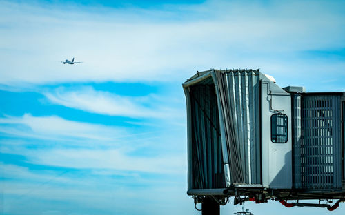 Jet bridge after commercial airline take off at the airport and the plane flying in the blue sky.