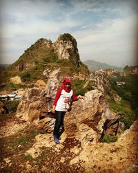 Portrait of young woman standing on cliff against sky