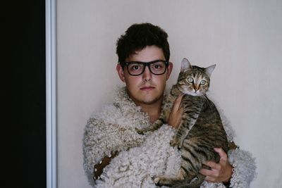 Portrait of man holding cat against wall