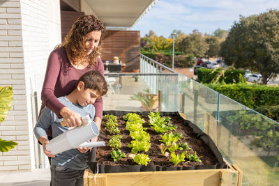 Mother and son watering vegetables in their urban garden