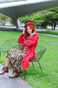 Young happy woman with red hair, freckles, beret, coat walking in autumn park, drinking coffee