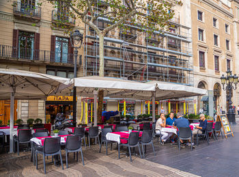 Chairs and tables at sidewalk cafe by buildings in city