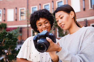 Smiling teenage girls holding camera while standing outdoors