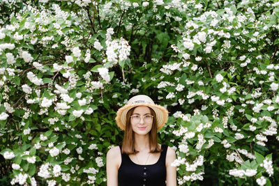 Portrait of young woman standing by flower tree