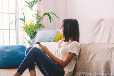 Woman with smart phone looking away at home