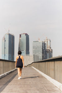 Woman exercise walking on the bridge hand holding bottle water with city building view.