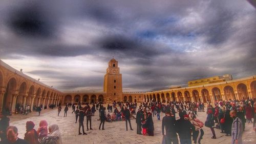 Group of people in front of historical building against cloudy sky