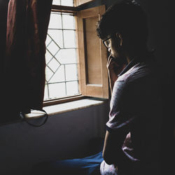 Side view of young man looking through window at home