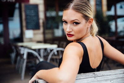 Portrait of confident young woman sitting on bench in city