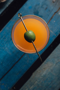 Carrot orange drink with green olive on cocktail pick against blue wood 