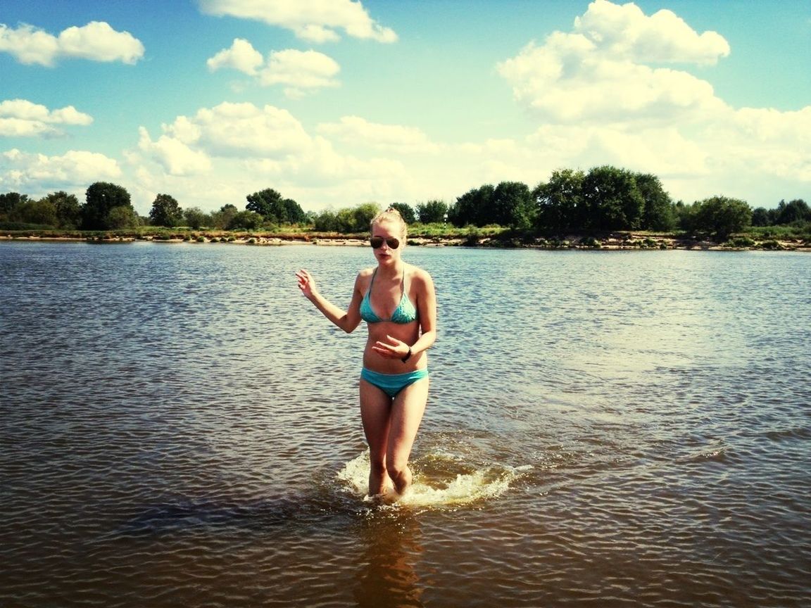 water, full length, sky, lifestyles, casual clothing, person, leisure activity, lake, standing, waterfront, tree, young adult, cloud - sky, tranquility, nature, river, cloud, rippled