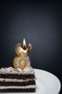 Lit candle on cake against gray background