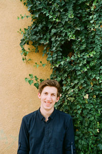 Portrait of smiling young woman by plants against wall