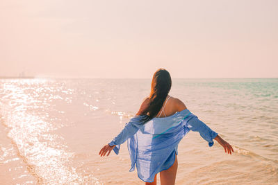 Rear view of woman standing at beach against sky