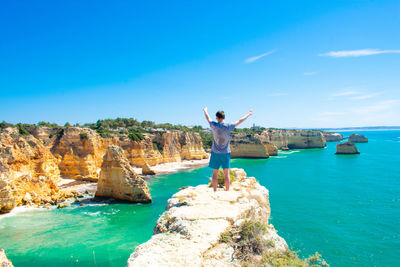 Rear view of man standing on rock by sea against sky