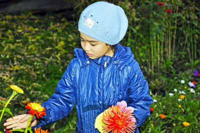 Girl wearing warm clothing while picking flowers in yard