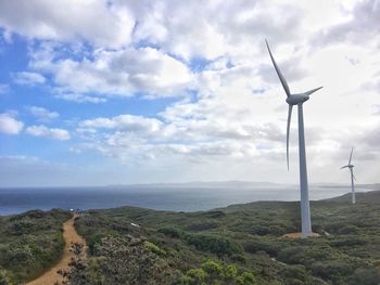 Wind turbines on field by sea against sky