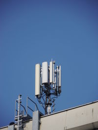 Low angle view of antennas on building terrace against clear blue sky