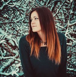 Thoughtful beautiful woman standing against snow covered bare tree