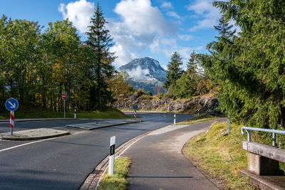 Road by trees against sky and alpine mountain