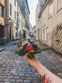 Woman holding flowers on footpath by street against buildings