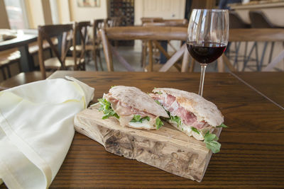 Side-view of an italian prosciutto sandwich on board and glass of wine